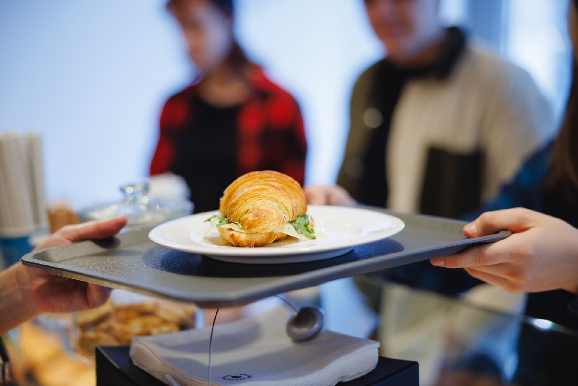 Taking tray with croissant sandwich on a plate in cafeteria in city street